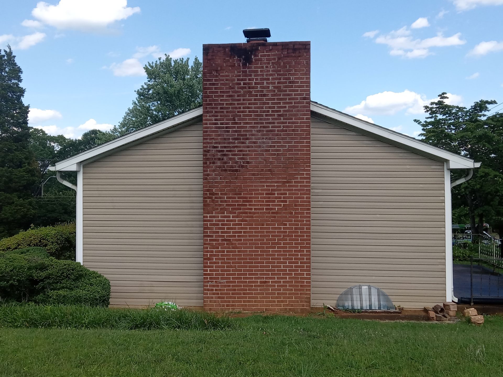 in this image the pressure washing service is being done on the exterior walls of a residential building the surfaces being cleaned include the siding which appears to be vinyl and also the brick facade around the chimney this type of pressure washing generally involves removing dirt mildew and algae to restore the appearance of the home's exterior