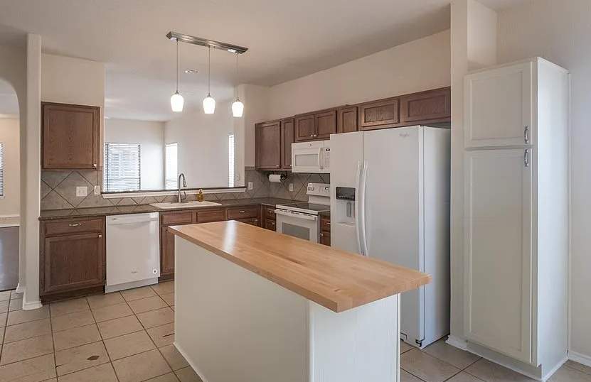 The old kitchen had a traditional builder-grade look with heavier wood cabinetry and busier finishes, while the new kitchen has a warm transitional design with cleaner lines, a brighter palette, and a more open, modern layout by Mena stone surfaces