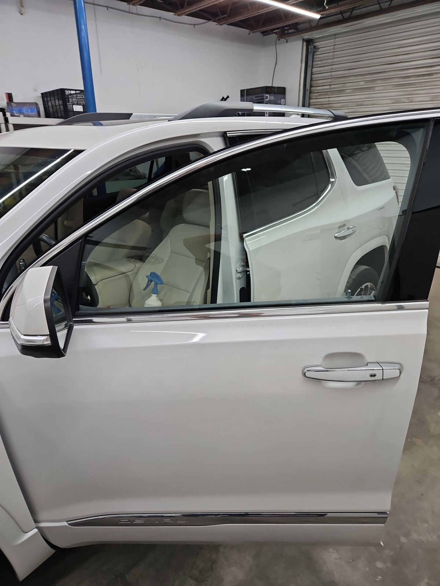 the service being done is the application of window tint on a vehicle the car appears to be a white model with a spacious interior and the technician is preparing the window for tinting using a spray bottle likely for cleaning or moisture this process aims to reduce heat and glare while providing privacy for passengers and protecting the interior from uv damage