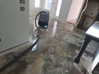 Wet concrete floor inside a home with extraction equipment and a hose running across the room.