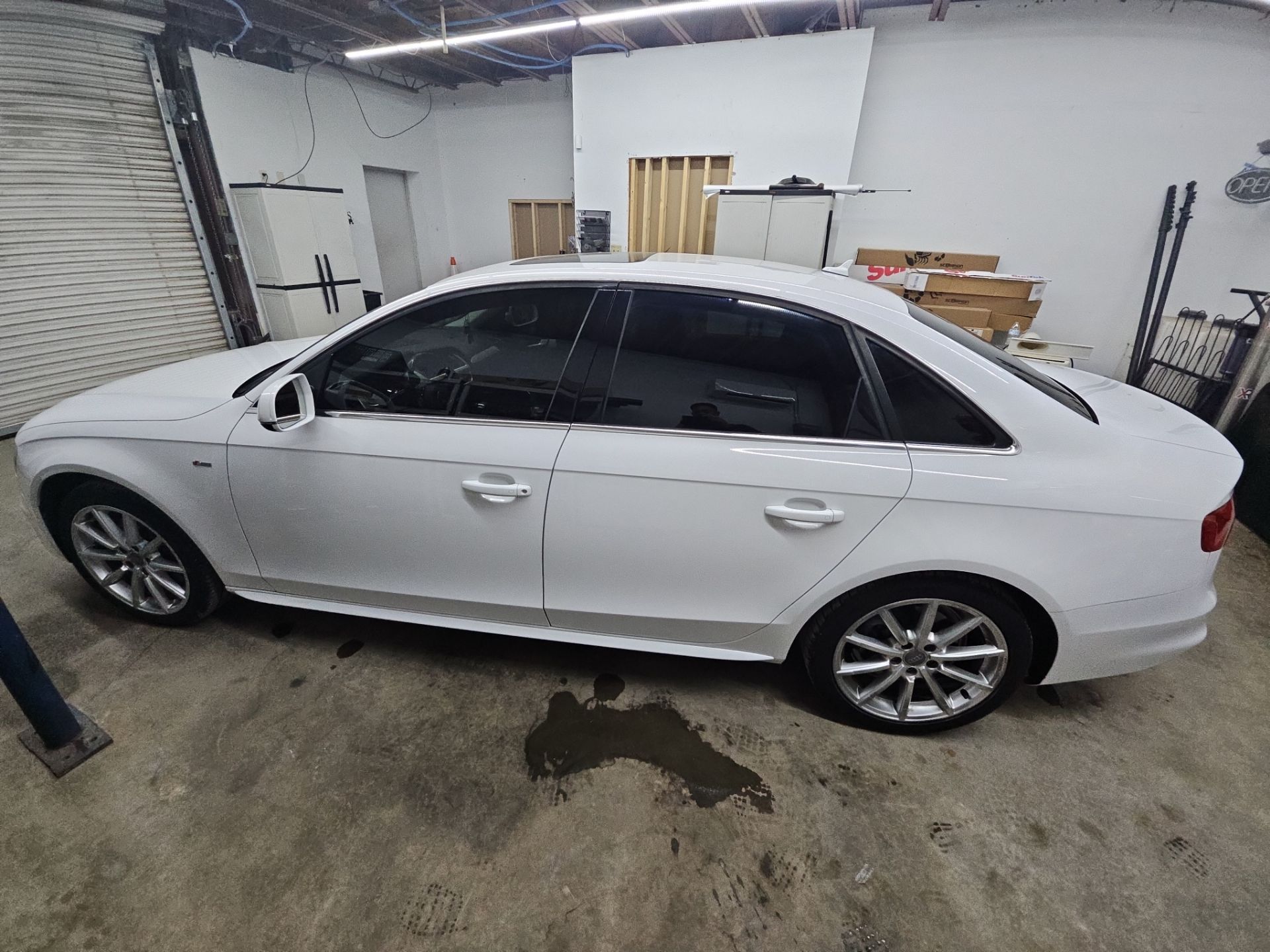 the image shows a white sedan that is being fitted with window tint by t's window tinting the service involves applying a dark film to the car's windows this helps reduce glare and heat while enhancing privacy the car appears to be in a garage setting likely indicating that the work is being done in a controlled environment ensuring a clean application process the visible windows are already tinted suggesting that the installation is either completed or near completion