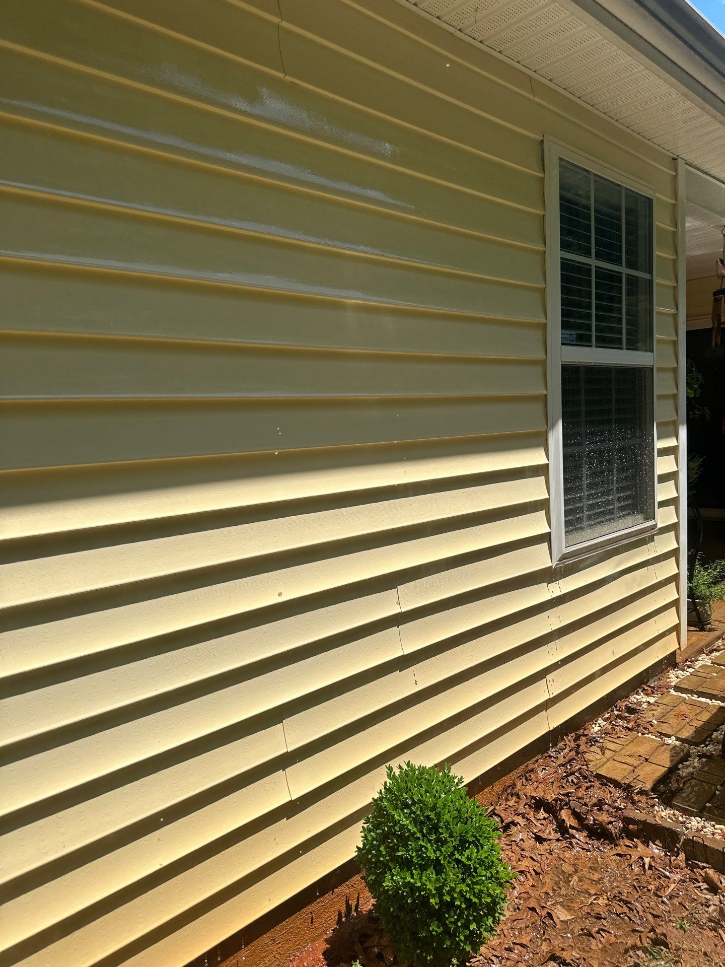 the photo shows a section of house siding where pressure washing is being performed the service being done is cleaning the exterior surface of a house where dirt and possibly mildew have built up over time the pressure washer uses high velocity water spray to remove grime from the siding which looks like vinyl the difference between the cleaned and uncleaned sections is clearly visible indicating the effectiveness of the pressure washing process