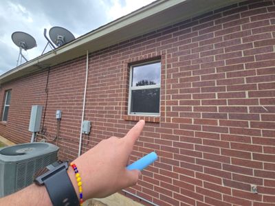 Hand pointing at window on brick exterior wall