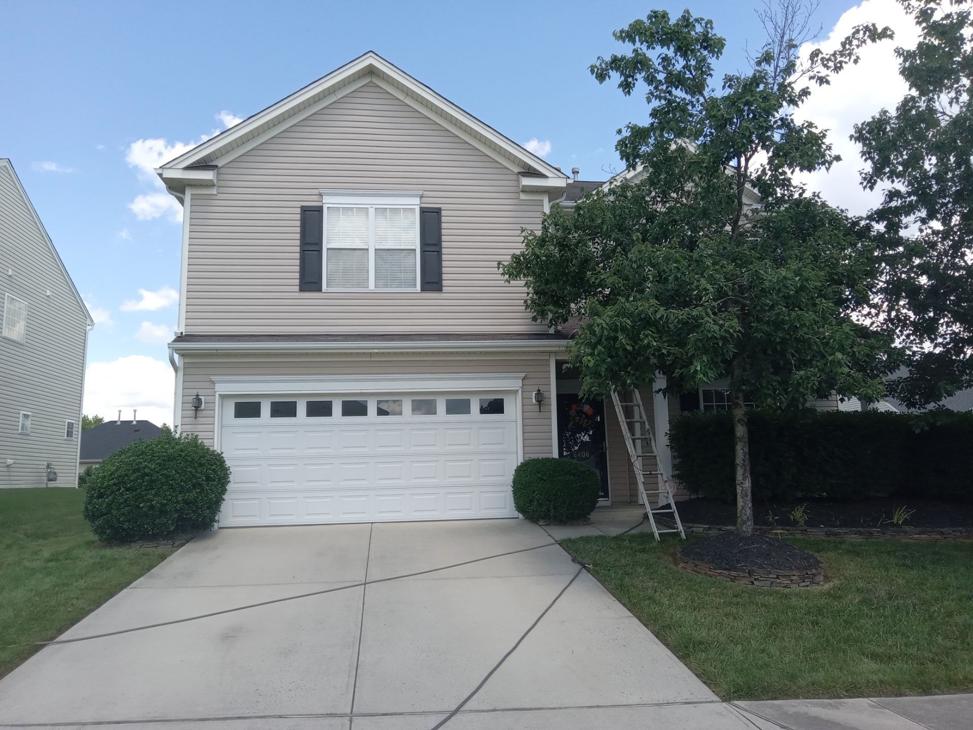 the image shows a two-story residential home with siding, a garage, and a driveway there is a ladder leaning against the house suggesting that the service being performed could include cleaning the siding or perhaps the gutters there is no visible pressure washing equipment or activity at the moment but given the context it is likely that the company might be pressure washing the home's siding the driveway and walkways or a combination of these surfaces pressure washing can remove dirt mold mildew and other buildups from these surfaces restoring their appearance and preventing potential damage