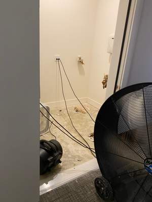 A large drying fan positioned near an open utility area with cords running across the floor.