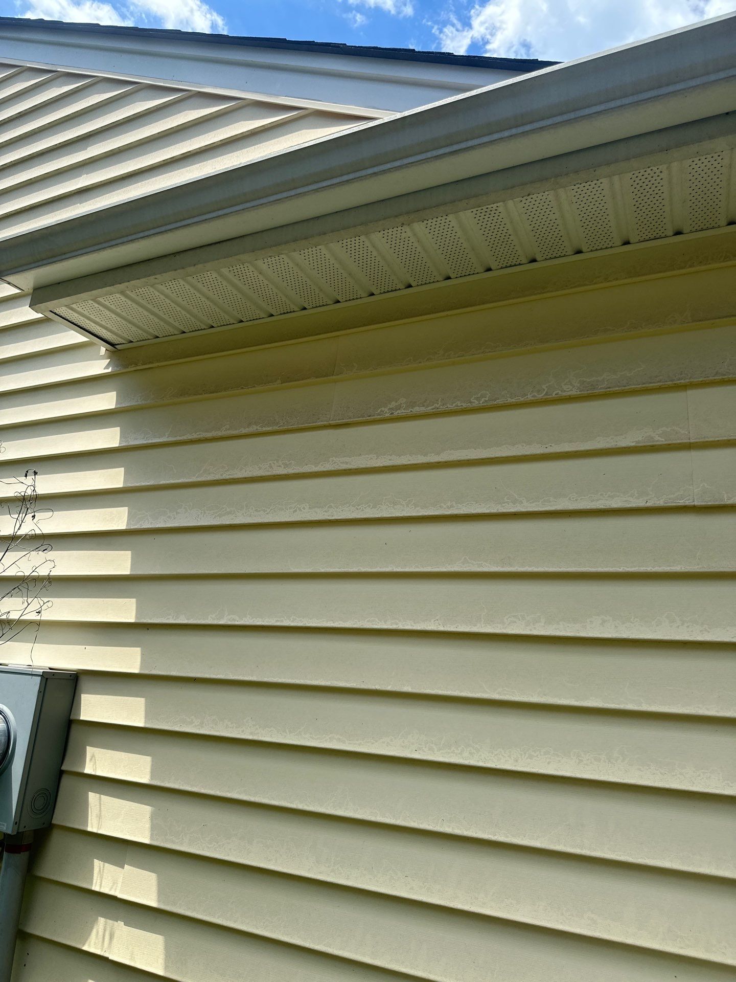 the pressure washing company is cleaning the exterior siding of a house the photo shows the difference between the cleaned area and the area that still has dirt and grime buildup the service involves using high-pressure water to remove dirt algae and possibly mildew from the siding for a refreshed and clean appearance the soffits under the roof also appear to be cleaned or due for cleaning this service improves the curb appeal and maintains the material condition of the home