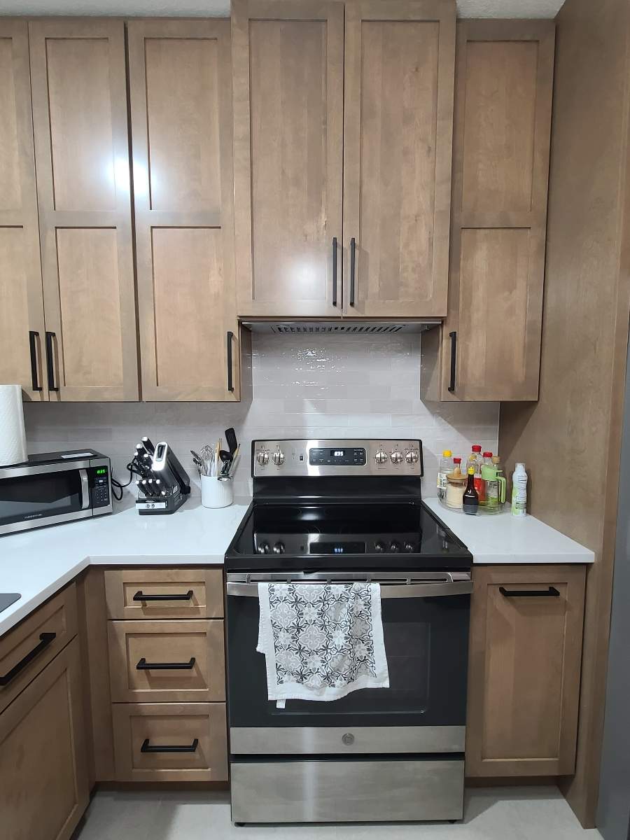 The old kitchen had a traditional builder-grade look with heavier wood cabinetry and busier finishes, while the new kitchen has a warm transitional design with cleaner lines, a brighter palette, and a more open, modern layout by Mena stone surfaces