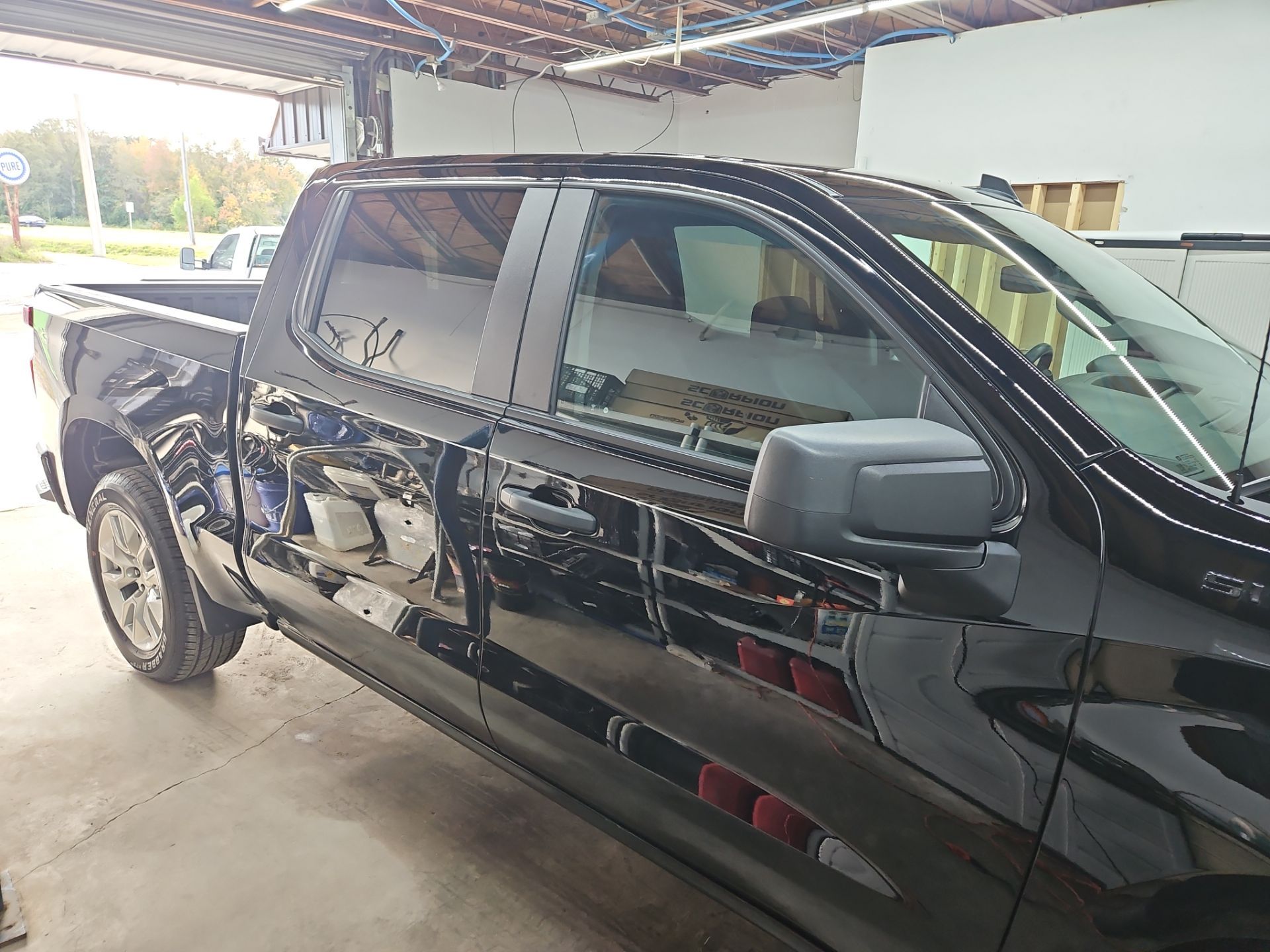 the image shows a black pickup truck that is having window tinting applied to its side windows the tinting process involves cleaning the windows to ensure a smooth application which helps in maintaining proper adhesion and enhancing the overall appearance the vehicle will have a darker tint for added privacy and protection from harmful uv rays this service is typical for improving the comfort and aesthetics of the vehicle