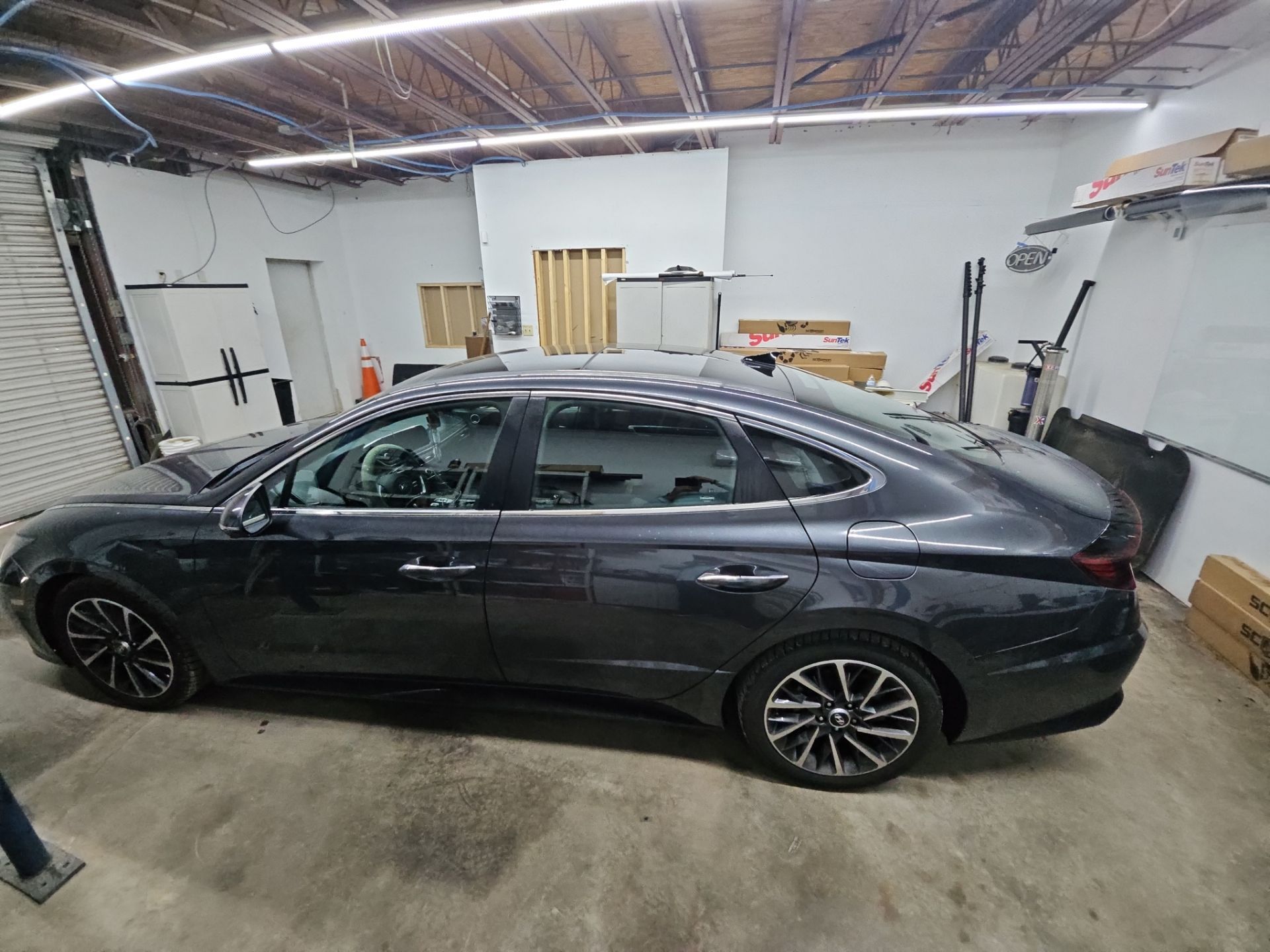 the service being done is window tinting on a dark gray sedan the car is likely being prepared for installation of tinted film on its windows the tinting will provide heat reduction and privacy for the vehicle's occupants the environment appears to be a professional tinting shop with tools and materials organized around the car the windows have been carefully cleaned to ensure proper adhesion of the tinting film