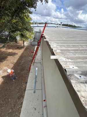 Worker on ladder near corrugated metal roof edge