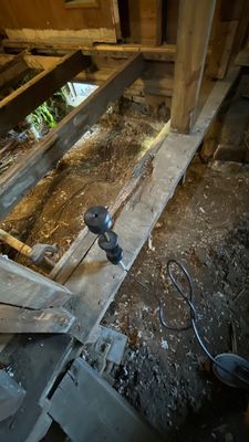 Crawlspace area with exposed floor joists, support framing, debris, a drill, and an electrical cord.