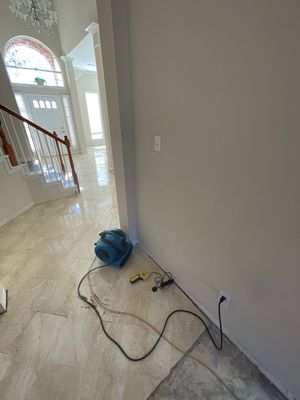 Blue air mover with cords placed along an interior wall near a bright entryway and staircase.