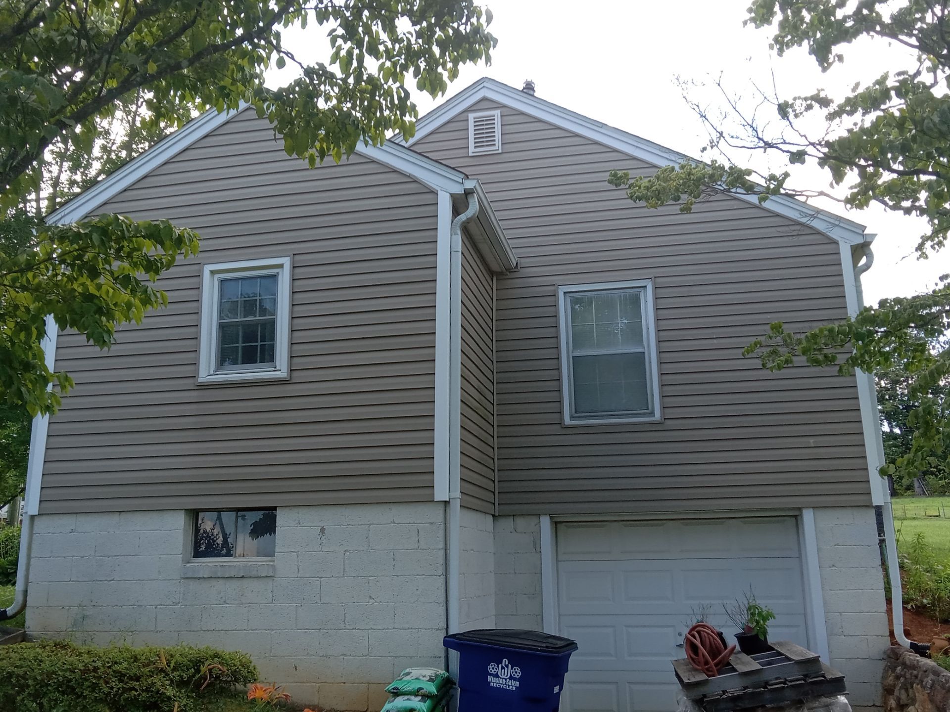 the pressure washing company is cleaning the exterior siding of a house the siding appears to be vinyl and is likely to have accumulated dirt mold or mildew which is common on home exteriors the pressure washing service is using high-pressure water to remove the unwanted substances from the siding restoring it to a cleaner and more aesthetically pleasing state they may also be cleaning the white gutters and downspouts as part of their service the lower part of the house has a concrete foundation which might also be included in the cleaning service to remove stains and build-up the photo does not show the cleaning process happening but it is implied by the context provided