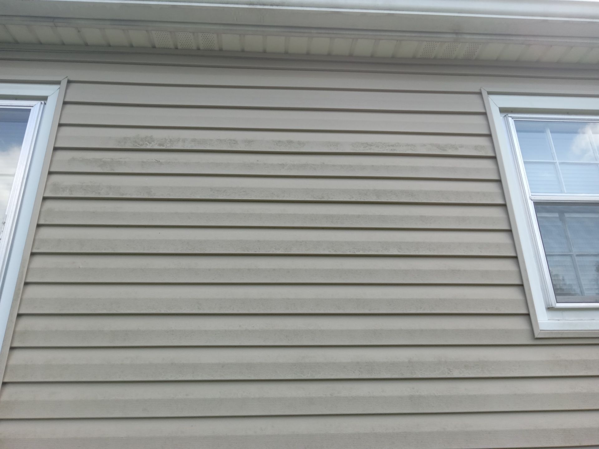 the pressure washing company is cleaning the exterior siding of a house the siding appears to be vinyl and shows signs of dirt and mildew accumulation the service involves using high-pressure water to remove the grime and restore the appearance of the siding the technique cleans the crevices and textured surfaces effectively leaving the home looking refreshed and well-maintained