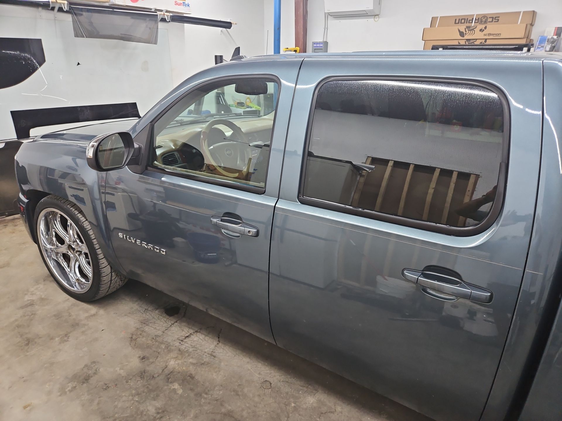 the service being performed is window tinting on a gray chevrolet silverado the windows appear to be receiving a dark tint which enhances privacy blocks uv rays and improves the vehicle's appearance the job is likely being done in a clean indoor environment to ensure a professional finish the vehicle's wheels suggest a customized look which is complemented by the new tinting