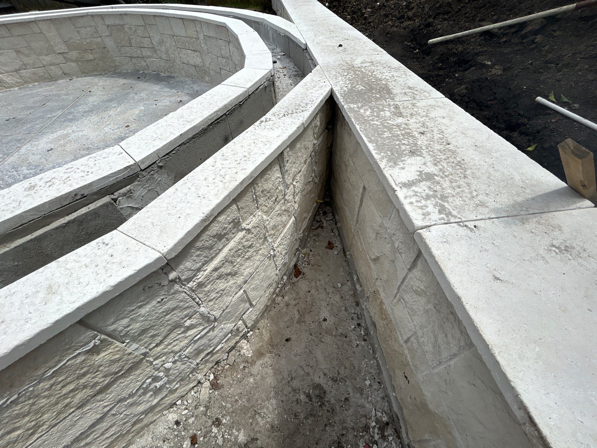 Major Transformation Project: Retaining Wall, Patio, and Drainage for Mr. & Mrs. Veerman! 🤩🛠️ We recently completed a comprehensive, custom project for Mr. & Mrs. Veerman that was all about structure, stability, and stunning outdoor design! This was a multi-phased project requiring the expertise of our Master Handcrafted Team.  Phase 1: Foundation and Water Management A successful outdoor space starts beneath the surface. We focused heavily on preparation and protection:  Demolition & Grading: We professionally removed and disposed of old dirt to achieve a level surface, ensuring the entire area was leveled and graded to enhance both appearance and functionality.  Comprehensive Drainage System: To prevent water issues and protect the new construction, we installed a complete system, connecting existing downspout gutters to channel drainage and strategically placed catch basins around the patio area.  Robust Concrete Foundation: Expert framing led to the pouring of a 4-inch deep, high PSI concrete slab to create a robust and lasting foundation for the entire retaining wall area.  Phase 2: Handcrafted Structure and Style This phase brought in our masonry and carpentry artisans to build the defining elements of the new space:  Custom Retaining Wall: Our master handcrafted team built a stunning, structural retaining wall. This involved careful framing, precise concrete work, and meticulous masonry construction with vertical supports every 3 feet for maximum stability.  Client Involvement: Mr. & Mrs. Veerman played a key role in selecting the retainer wall fascia and stone materials, ensuring the final look perfectly matched their vision.  Stamped Concrete Patio: We installed a beautiful stamped concrete patio. This decorative concrete work involved imprinting a pattern into the fresh concrete, giving them the high-end look of stone or brick with the durability of concrete.  Walk Add-On: Extended the stamped concrete to include a new, seamless walk area.  (Optional) Custom Garden Box: Constructed durable, raised garden boxes using 2"x12" boards and strong 4"x6" posts.  Phase 3: Landscaping and Finishing Touches The final details bring the entire project to life, focusing on irrigation and planting:  Sprinkler System Upgrade: To support their new landscaping, we upgraded their irrigation system by installing two new drip zones and a new control unit.  Flower Beds: Integrated new flower beds along the retaining wall and patio, ready for planting.  Decoration: Concluded the project with personalized decoration options to perfectly complement their beautiful, newly structured space.  Thinking About a Multi-Layered Outdoor Project? This project demonstrates our ability to seamlessly handle complex jobs—from heavy-duty drainage and structural construction to decorative finishes and irrigation.  The proposed timeline for this extensive project was 10 to 15 working days!  ❓ Do you have a sloping yard or drainage issues that could be solved with a functional and beautiful retaining wall? Tell us your challenge! 👇  💡 We specialize in bringing intricate outdoor visions to life! If you're looking for a team with master craftsmen for your next patio, retaining wall, or full landscape overhaul, let's talk. by Texas Urban Elements