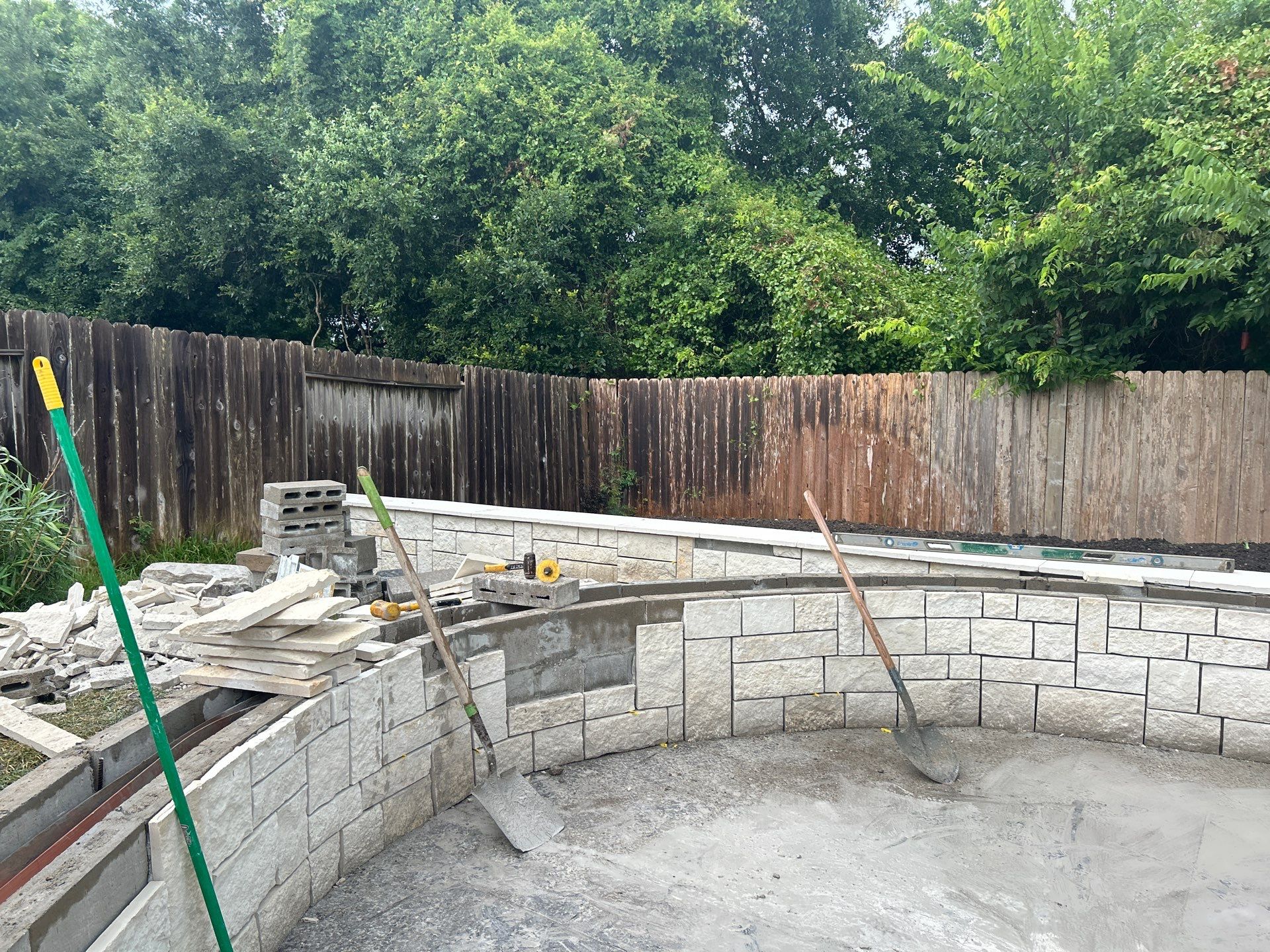 Major Transformation Project: Retaining Wall, Patio, and Drainage for Mr. & Mrs. Veerman! 🤩🛠️ We recently completed a comprehensive, custom project for Mr. & Mrs. Veerman that was all about structure, stability, and stunning outdoor design! This was a multi-phased project requiring the expertise of our Master Handcrafted Team.  Phase 1: Foundation and Water Management A successful outdoor space starts beneath the surface. We focused heavily on preparation and protection:  Demolition & Grading: We professionally removed and disposed of old dirt to achieve a level surface, ensuring the entire area was leveled and graded to enhance both appearance and functionality.  Comprehensive Drainage System: To prevent water issues and protect the new construction, we installed a complete system, connecting existing downspout gutters to channel drainage and strategically placed catch basins around the patio area.  Robust Concrete Foundation: Expert framing led to the pouring of a 4-inch deep, high PSI concrete slab to create a robust and lasting foundation for the entire retaining wall area.  Phase 2: Handcrafted Structure and Style This phase brought in our masonry and carpentry artisans to build the defining elements of the new space:  Custom Retaining Wall: Our master handcrafted team built a stunning, structural retaining wall. This involved careful framing, precise concrete work, and meticulous masonry construction with vertical supports every 3 feet for maximum stability.  Client Involvement: Mr. & Mrs. Veerman played a key role in selecting the retainer wall fascia and stone materials, ensuring the final look perfectly matched their vision.  Stamped Concrete Patio: We installed a beautiful stamped concrete patio. This decorative concrete work involved imprinting a pattern into the fresh concrete, giving them the high-end look of stone or brick with the durability of concrete.  Walk Add-On: Extended the stamped concrete to include a new, seamless walk area.  (Optional) Custom Garden Box: Constructed durable, raised garden boxes using 2"x12" boards and strong 4"x6" posts.  Phase 3: Landscaping and Finishing Touches The final details bring the entire project to life, focusing on irrigation and planting:  Sprinkler System Upgrade: To support their new landscaping, we upgraded their irrigation system by installing two new drip zones and a new control unit.  Flower Beds: Integrated new flower beds along the retaining wall and patio, ready for planting.  Decoration: Concluded the project with personalized decoration options to perfectly complement their beautiful, newly structured space.  Thinking About a Multi-Layered Outdoor Project? This project demonstrates our ability to seamlessly handle complex jobs—from heavy-duty drainage and structural construction to decorative finishes and irrigation.  The proposed timeline for this extensive project was 10 to 15 working days!  ❓ Do you have a sloping yard or drainage issues that could be solved with a functional and beautiful retaining wall? Tell us your challenge! 👇  💡 We specialize in bringing intricate outdoor visions to life! If you're looking for a team with master craftsmen for your next patio, retaining wall, or full landscape overhaul, let's talk. by Texas Urban Elements