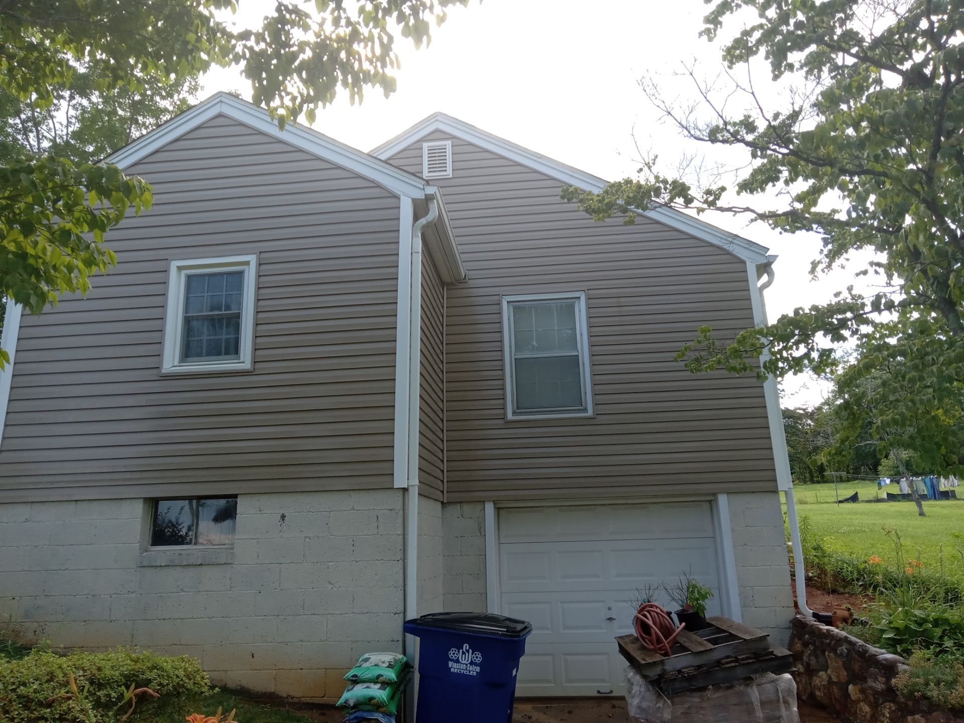 the image shows the exterior of a two-story house with vinyl siding the pressure washing service likely involves cleaning the siding to remove dirt mold and mildew buildup the lower portion of the house shows a cinder block foundation that might also be cleaned to remove any stains or growths this type of service helps to maintain the exterior of the home and can refresh its appearance improving curb appeal