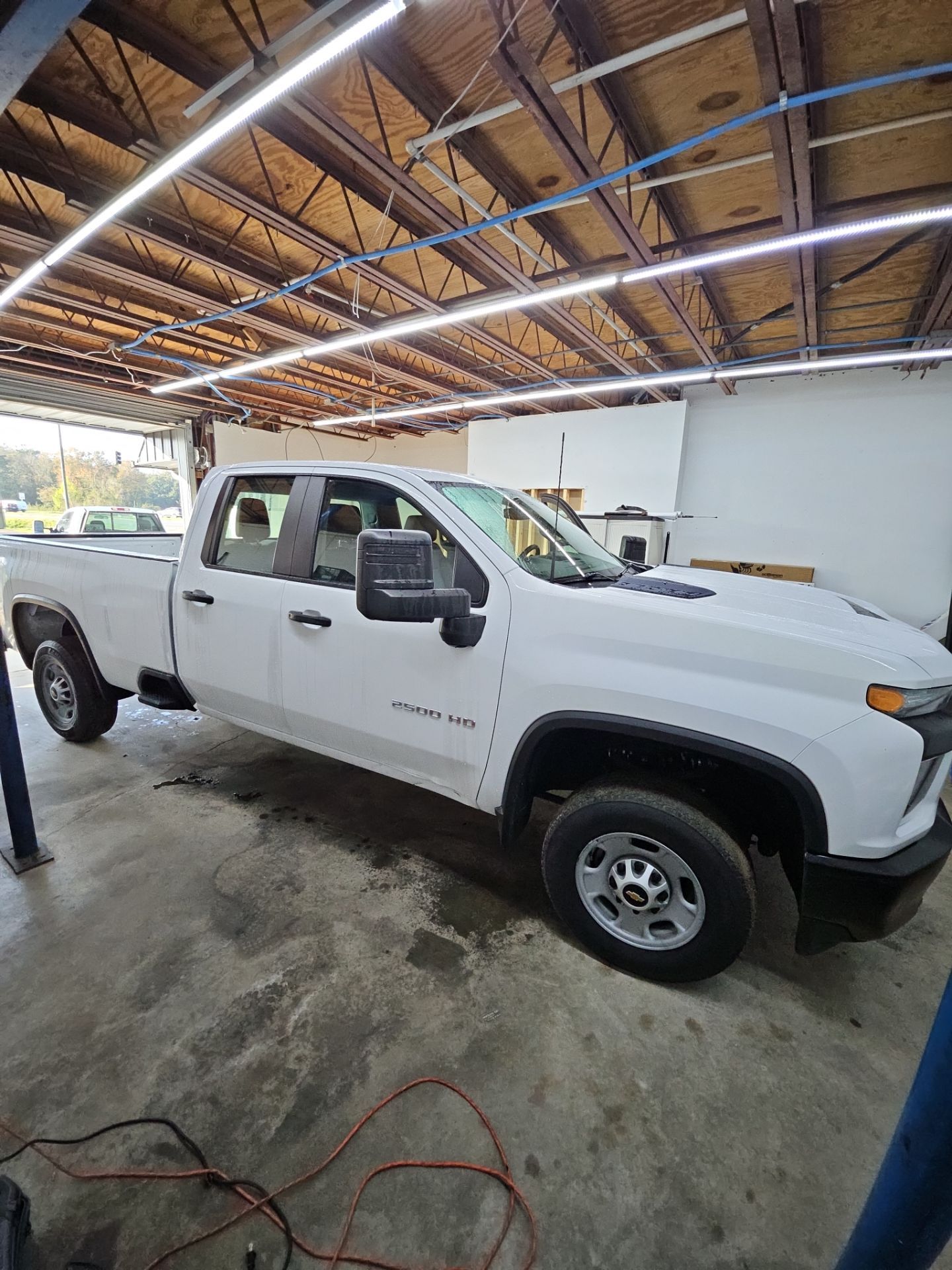 the image shows a white pickup truck likely undergoing a cleaning service before window tinting the vehicle the truck appears to be a heavy duty model and is inside a workshop designed for automotive services the area is well lit and the floor shows signs of water or cleaning materials indicating preparations for the tinting process the focus is on ensuring the surface is clean for optimal adhesion of the window tint.