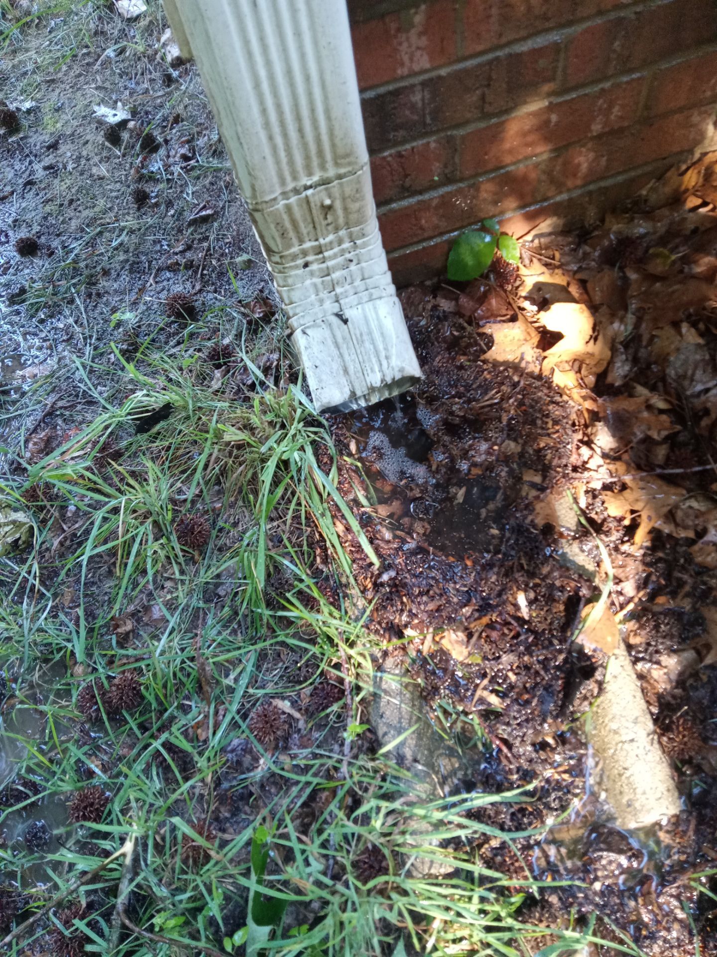 pressure washing to clean dirt and buildup from vertical downspout and brick wall base near ground level