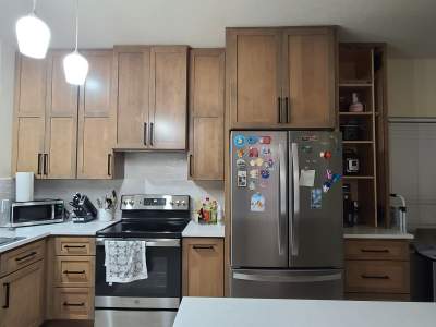The old kitchen had a traditional builder-grade look with heavier wood cabinetry and busier finishes, while the new kitchen has a warm transitional design with cleaner lines, a brighter palette, and a more open, modern layout by Mena stone surfaces