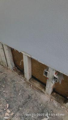 Close-up of a lower wall section with drywall removed, exposing studs, insulation, and an electrical outlet.