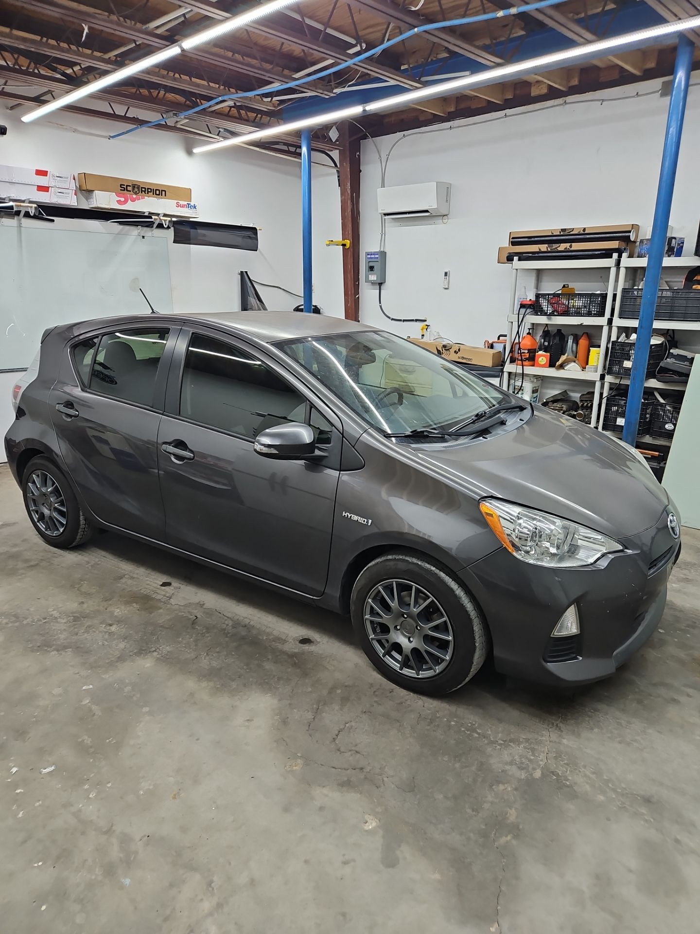 the service being performed is window tinting on a gray hatchback car the technicians are likely applying a film to the windows to reduce glare improve privacy and block harmful uv rays the car is parked in a workshop environment indicating a professional setting for this service the tinting process typically involves cleaning the windows meticulously measuring the film and carefully applying it to ensure a smooth and even finish