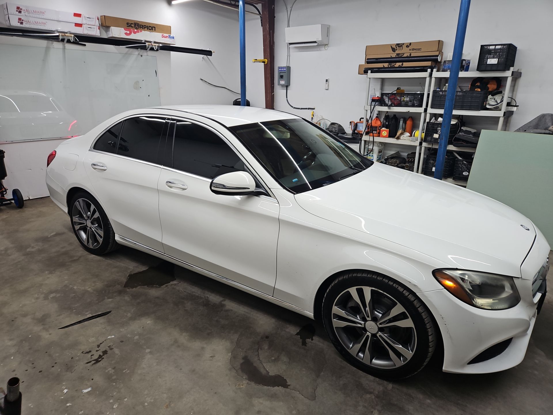 the image shows a white car that is undergoing window tinting service in a shop the car has recently been cleaned and is likely being prepared for the application of window film the tinting will help reduce heat inside the vehicle and provide privacy for the occupants the process involves careful measurement and cutting of the film to fit the windows the finished product enhances the overall appearance of the car while also providing functional benefits