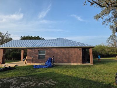 Worker handling blue tarp on a metal roof project.