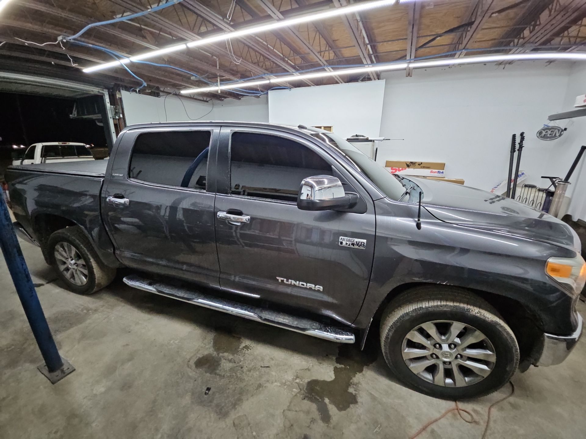 the photo shows a grey toyota tundra parked inside a shop where window tinting service is being performed the windows appear to have tint applied already giving the vehicle a sleek look the truck likely benefits from reduced glare increased privacy and protection from harmful uv rays the tinting is done professionally as indicated by the even application and the clean lines around the edges the vehicle is positioned in a well-lit garage setting suggesting that the service is being handled attentively