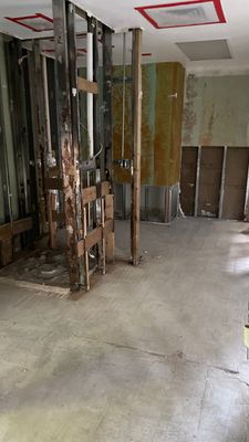 Commercial interior room with sections of wall material removed, exposed framing, and a concrete floor.