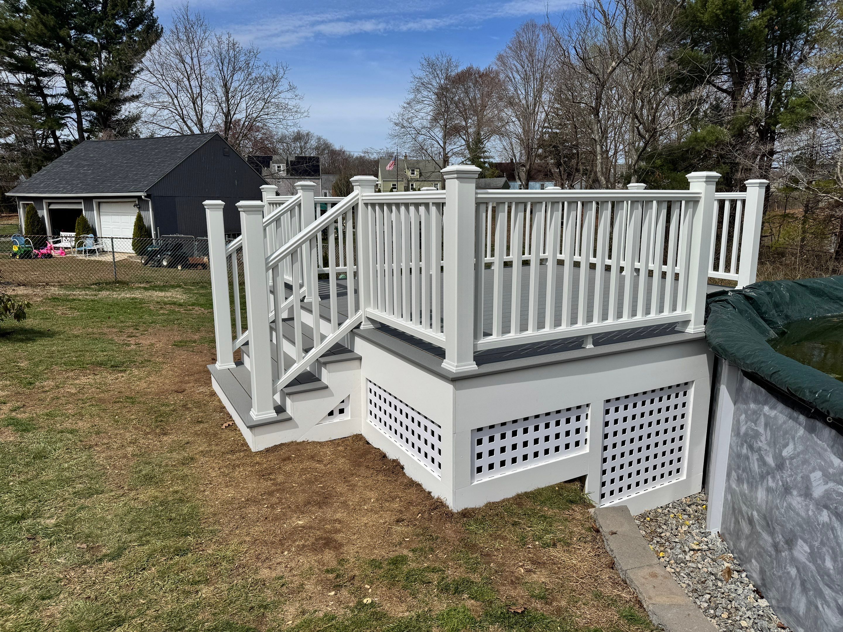New pool deck using Trex Pebble Gray boards and White composite railings and lattice  by DiGiorgi Roofing and Siding Inc