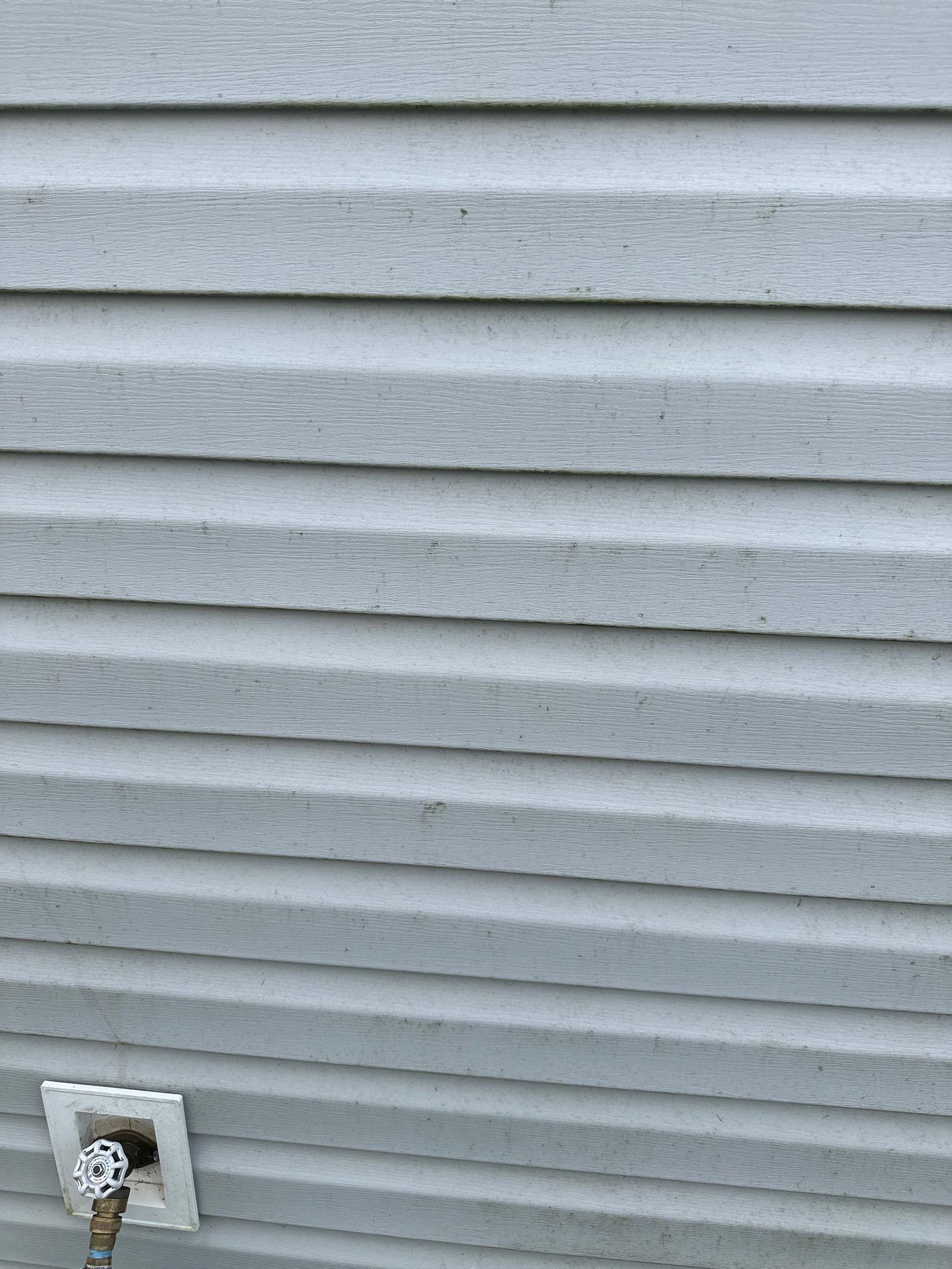 the photo shows a section of vinyl siding on a building the siding is textured with horizontal lines indicating the individual panels there are subtle signs of dirt and mildew which are common on exterior surfaces exposed to the elements the pressure washing service is being performed to clean these surfaces effectively removing dirt buildup algae mold and other stains that can accumulate over time the high-pressure water stream provided by the pressure washing equipment is powerful enough to clean the surface without the need for abrasive cleaning techniques maintaining the integrity of the siding while restoring its appearance to a cleaner state