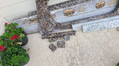 Close-up view of an exterior threshold area with stone or concrete surface, planters, and trim pieces.